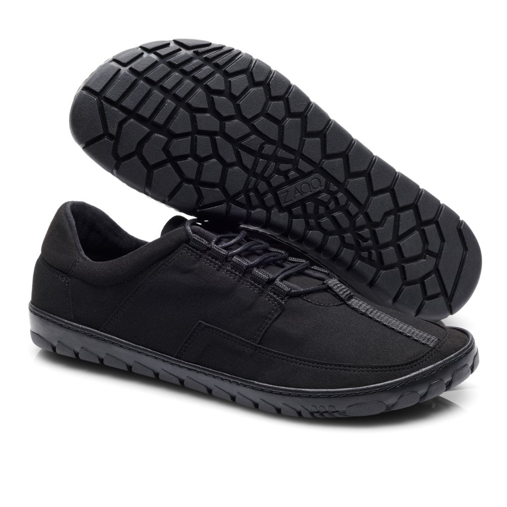 Wir präsentieren die JAQ Vegan Black Sneaker von ZAQQ. Diese schwarzen veganen Sneaker zeichnen sich durch ein minimalistisches Design mit strukturierten Kautschuksohlen für besseren Halt aus. Ein Schuh steht aufrecht, während der andere auf der Seite liegt, wodurch das markante Profilmuster hervorgehoben wird.