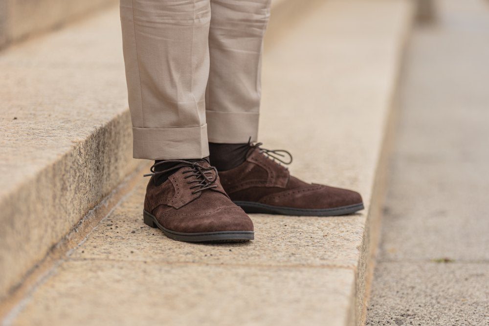 Eine Person in hellbeiger Hose und den eleganten ZAQQ BRIQ Brogue Velours Brown steht auf Steinstufen. Der Fokus liegt auf den Schuhen, gefertigt aus exquisitem französischem Kalbleder, sowie dem unteren Teil der Hose.