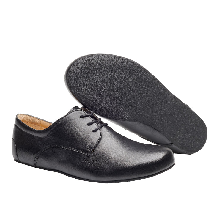 Der IQON Black von ZAQQ ist ein Paar eleganter schwarzer Lederschuh, ideal für ein elegantes Business-Outfit. Ein Schuh steht aufrecht und betont die Oberseite, während der andere auf der Seite liegt und die glatte Sohle zeigt. Diese stilvollen Schuhe zeichnen sich durch einen klassischen Derby-Schnitt mit Schnürsenkeln und einem flachen Design aus.