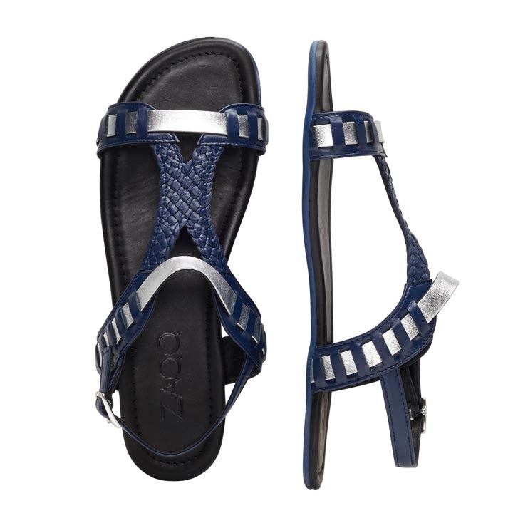 Zwei dunkelblaue Sandalen aus der BLINQ-Kollektion von ZAQQ mit geflochtenen Riemen, silbernen Akzenten und einer Kautschuksohle sind auf einem weißen Hintergrund platziert. Eine Sandale ist von oben zu sehen, während die andere ihr Barfußsandale-Design von der Seite zeigt und sowohl Stil als auch außergewöhnlichen Tragekomfort zeigt.