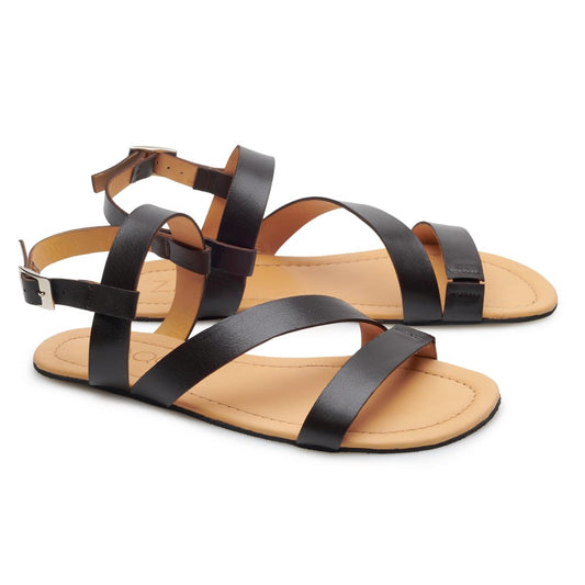 Die NIQ Dark Brown Sandalen von ZAQQ sind aus weichem Nappaleder gefertigt und verfügen über Riemchendetails aus schwarzem Leder, flache Sohlen und Knöchelriemen und bieten einen eleganten Look vor weißem Hintergrund.