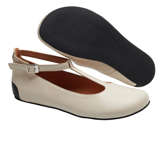 Die QITE Beige Ballerinas von ZAQQ sind ein schickes Paar Damenschuhe aus hochwertigem Nappaleder mit T-Riemen und Schnallenverschluss. Diese modischen Schuhe haben eine cremefarbene Farbe mit schwarzer Sohle und Absatz, ergänzt durch ein elegantes, abgerundetes Zehendesign. Das Bild zeigt einen Schuh nach oben, während der andere seine Sohle zeigt.