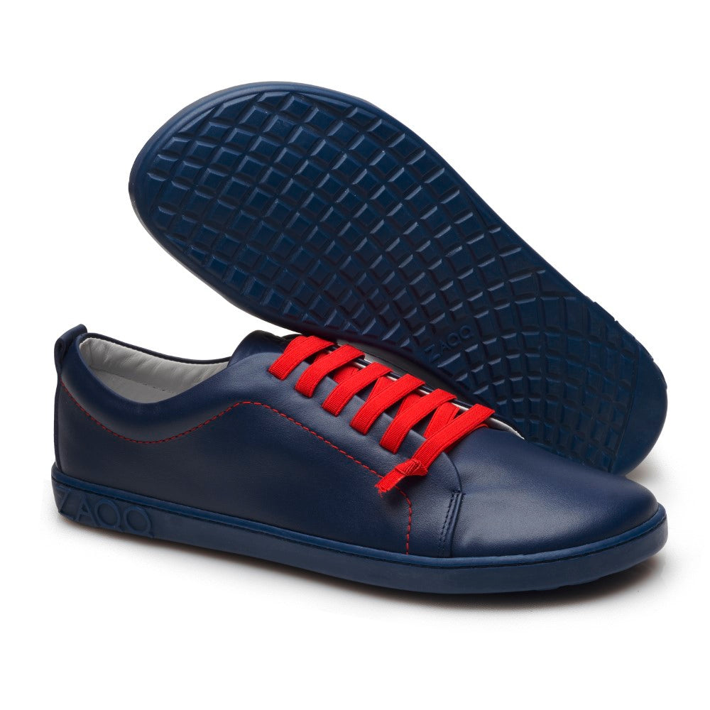 Ein Paar schicke STIQ Navy-Sneaker von ZAQQ, mit modernem, minimalistischem Design, leuchtend roten Schnürsenkeln und einer Kautschuksohle. Ein Schuh steht aufrecht, während der andere geneigt ist, um seine strukturierte Sohle aus hochwertigem Nappaleder zu präsentieren.