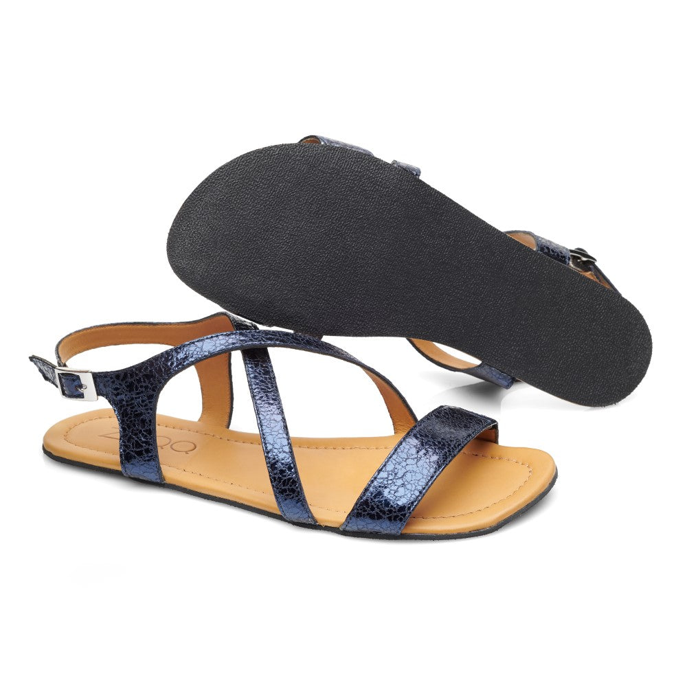 Wir präsentieren die ZAQQ Damensandalen mit strukturierten QEE-Blue-Riemen und hellbraunem Fußbett, die mit einem stilvollen Schnallenverschluss ausgestattet sind. Eine Sandale ist elegant von der Seite zu sehen, während die andere ihre schwarze Sohle zur Schau stellt und das schicke Design dieser Barfuß-Sandale unterstreicht.