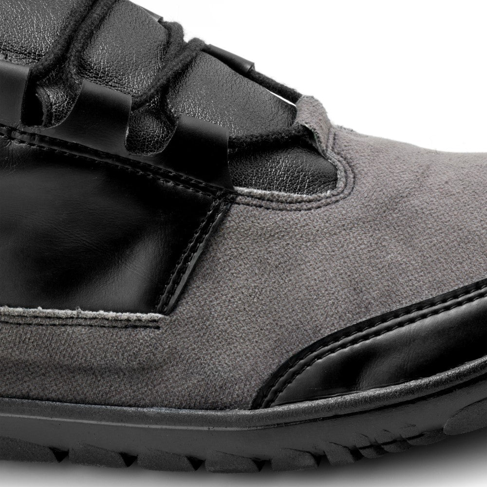 Nahaufnahme des QUEST Low Black Waterproof von ZAQQ mit einem Obermaterial aus strukturiertem grauem Stoff mit Akzenten und Schnürsenkeln aus glattem schwarzem Leder. Die schwarze Sohle, die für Grip sorgt, weist sichtbare Rillen auf. Das Bild hebt den Kontrast zwischen den Materialien hervor und verkörpert sowohl Stil als auch Funktionalität.