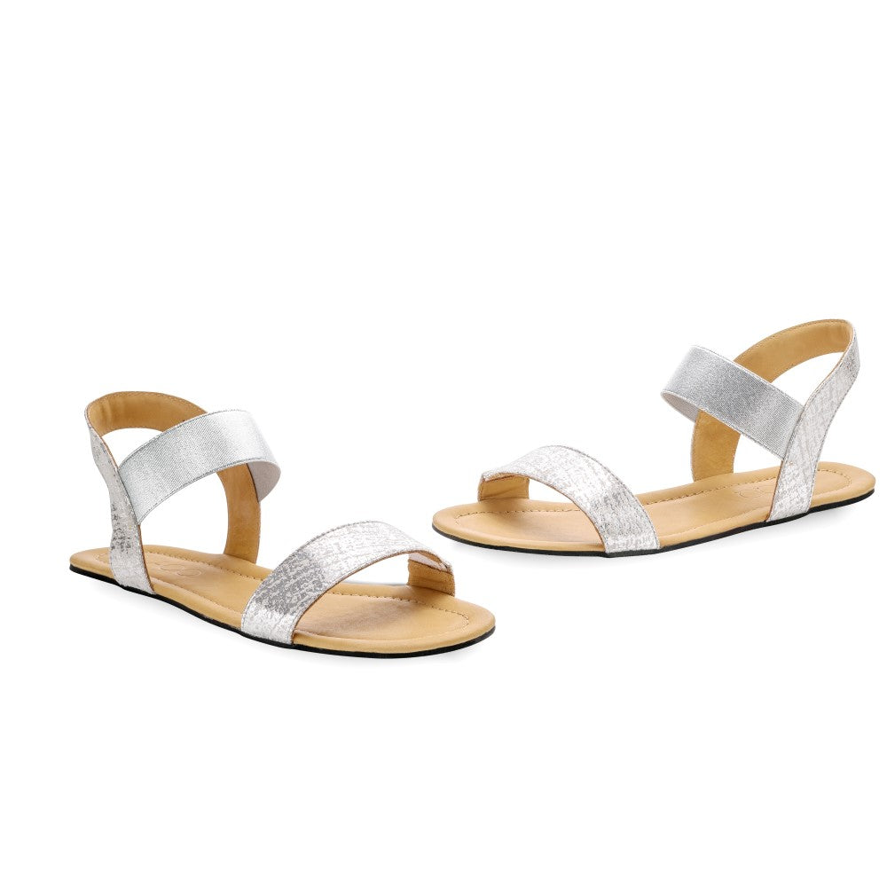 Entdecken Sie die SLIQ-Silver-Sandalen von ZAQQ, eine minimalistische Riemchensandale, die sorgfältig aus hochwertigem Nappaleder gefertigt wurde. Diese stilvollen silbernen Sandalen zeichnen sich durch breite Knöchel- und Zehenriemen sowie eine glatte, flache beige Sohle aus, die sich wunderschön vor einem makellos weißen Hintergrund präsentieren.